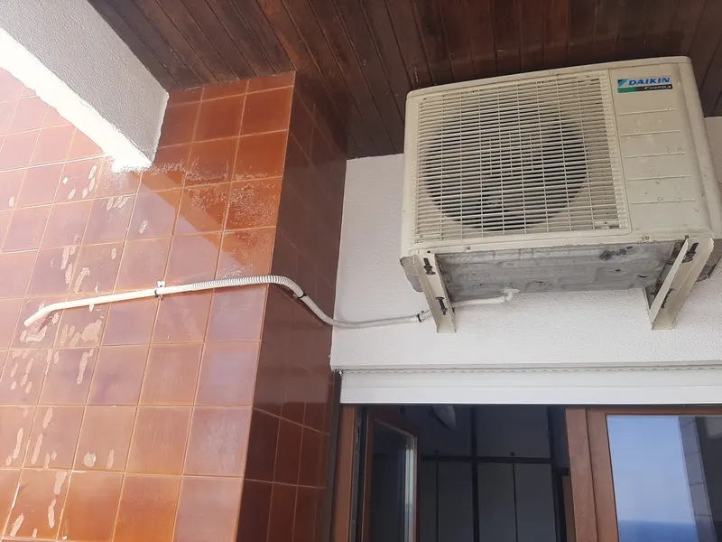 Unidade exterior de ar condicionado instalada por cima de uma porta em Lisboa, com a tubagem protegida ao longo da parede de azulejo.