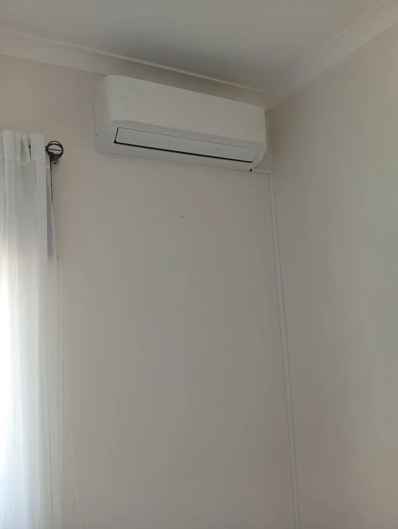 Unidade interior de ar condicionado instalada no alto de uma parede, junto à janela, numa casa em Odivelas.