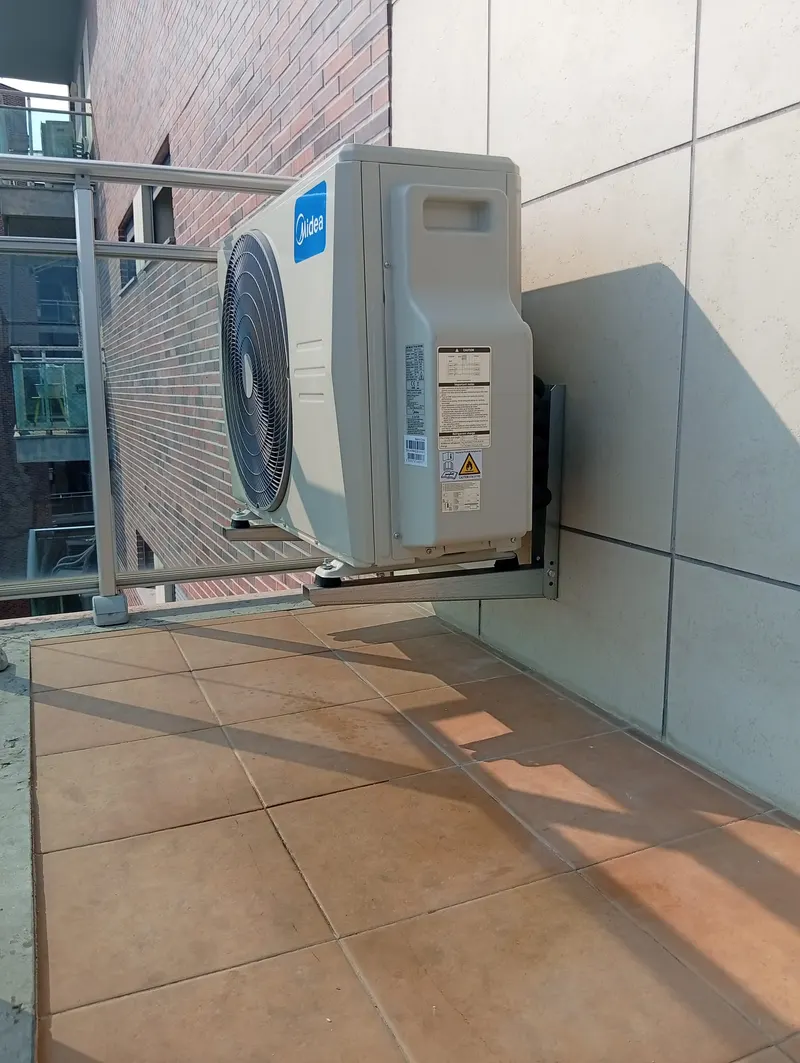 Unidade exterior de ar condicionado fixada na parede de uma varanda com guarda de vidro, em Oeiras.