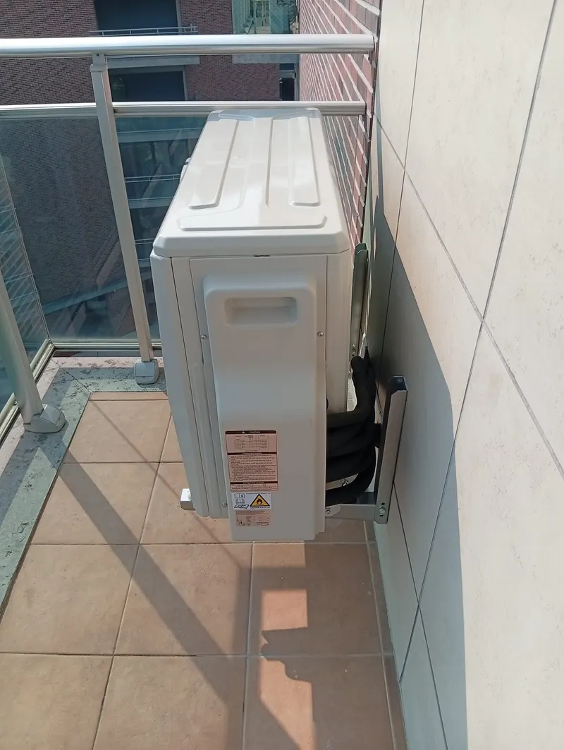 Unidade exterior de ar condicionado instalada num canto da varanda de um apartamento em Oeiras.