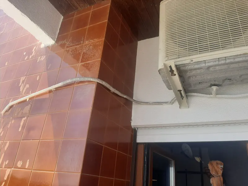 Pormenor de unidade exterior de ar condicionado sobre uma porta em Lisboa, com a ligação da tubagem à vista.