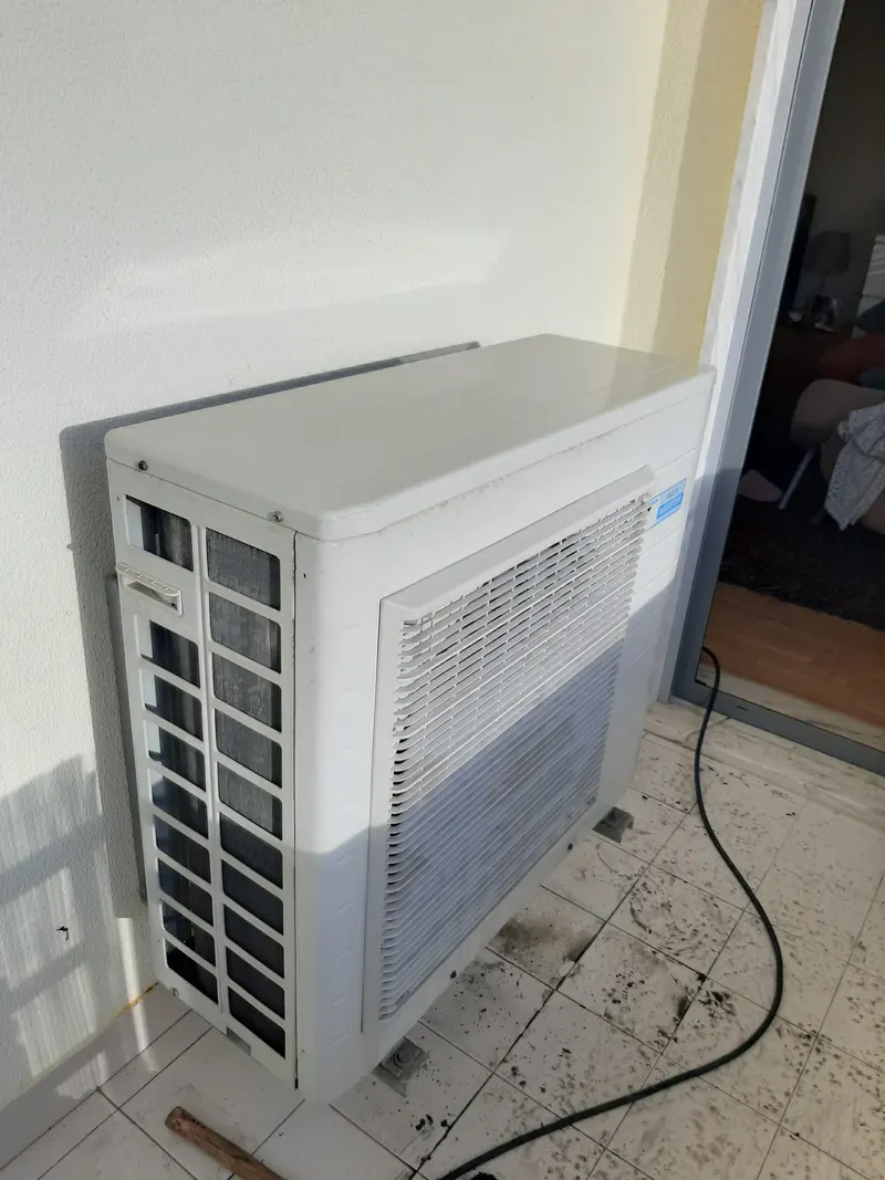 Unidade exterior de ar condicionado pousada no chão de uma obra na Amadora, antes da instalação.