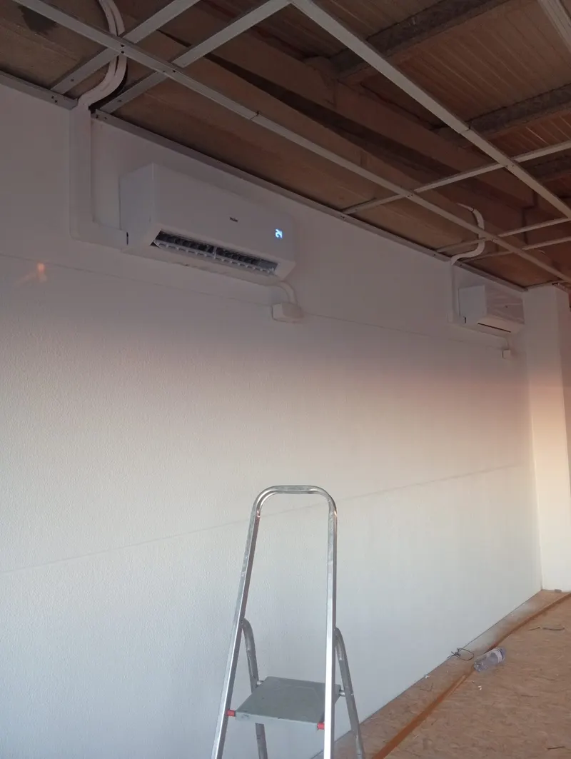 Unidade interior de ar condicionado numa sala com teto de vigas em Arruda dos Vinhos, com o escadote ainda no local.