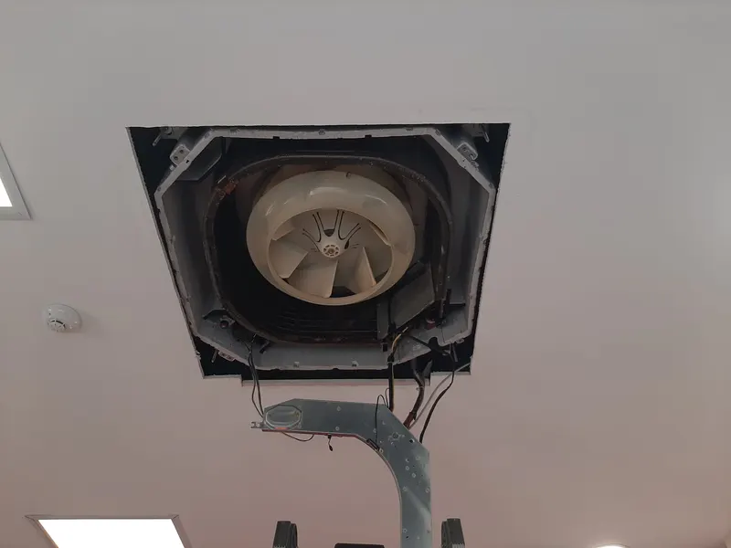 Ar condicionado de cassete no teto, com a grelha retirada e o ventilador à vista.