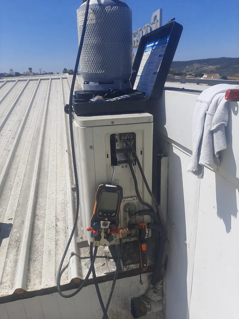 Manómetros ligados à unidade exterior de ar condicionado, com garrafa de gás refrigerante num terraço.